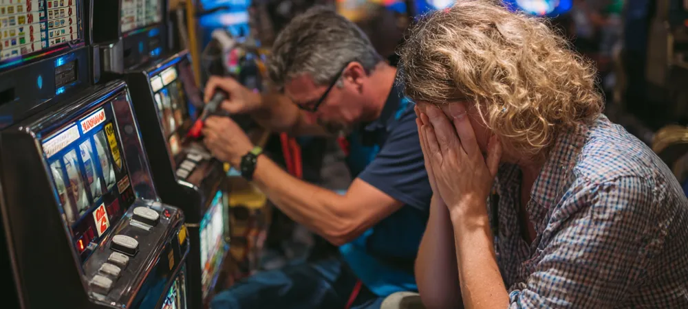 repairmen tinkering with a slot machine and person being angry to lose